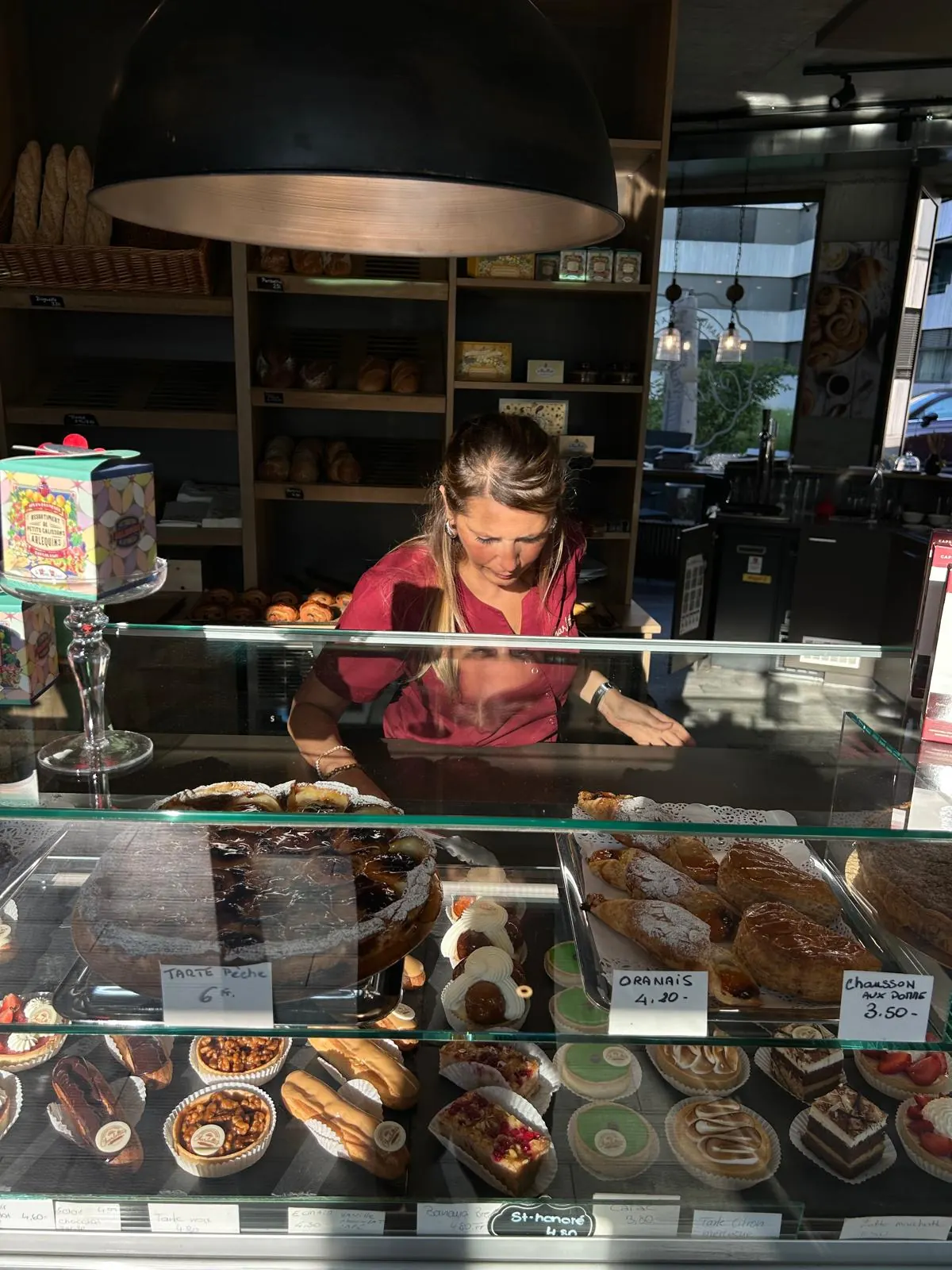 Charlotte derrière la vitrine de la boutique, pâtisseries et pains